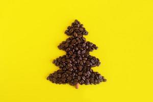 Winter composition with Christmas tree made by coffee beans and decorated cinnamon stick on a yellow background, flat lay. Greeting card for New Year with copy space. photo