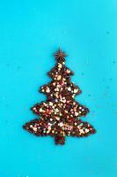 Christmas tree made from coffee beans and decorated anise star and multicolored culinary sprinkling on a blue background, top view. photo