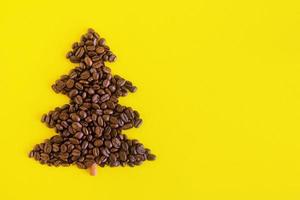 Winter composition with Christmas tree made by coffee beans and decorated cinnamon stick on a yellow background, flat lay. Greeting card for New Year with copy space. photo