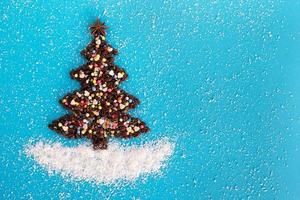 Christmas tree made from coffee beans and decorated anise star, multicolored culinary sprinkling and coconut chips on a blue background, top view. photo