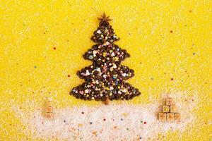 Christmas tree made from coffee beans and Christmas gifts made from waffles decorated coconut chips, anise star and multicolored culinary sprinkling on a yellow background, top view. photo