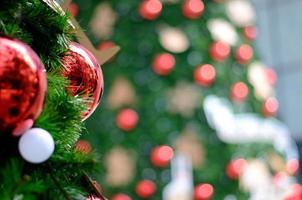 Red bauble and other ornament hanging on Christmas tree with bokeh background from another Christmas tree photo