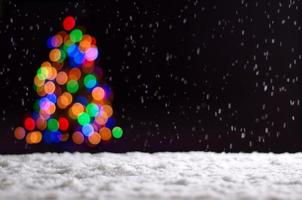 coloridas luces de bokeh del árbol de navidad cuando nieva en el suelo. foto