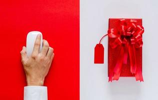 mano usando el mouse comprando en línea con caja de Navidad roja y etiqueta de precio sobre fondo blanco y rojo. concepto de lunes cibernético. foto