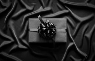 A black gift box with ribbon puts on black wavy cloth. Black friday and Boxing day concept. photo
