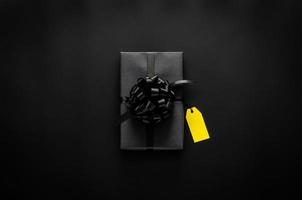 una caja de regalo negra con cinta y una etiqueta de precio en blanco amarilla se pone sobre fondo negro. concepto de viernes negro y día de boxeo. foto