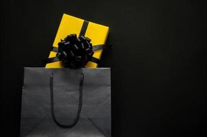 A yellow gift box puts in black shopping bag with black background. Black friday and Boxing day concept. photo