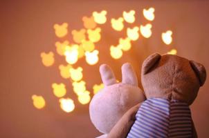 Teddy bear and rabbit dolls acting as lover sitting together to watch bear shape bokeh light background that have space for text.