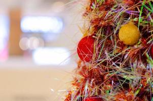 Red and gold baubles hanging on colorful Christmas tree with blurred background with space for text. photo