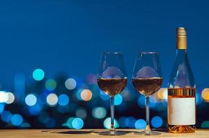 Two glasses and bottle of Rose wine with bokeh city colorful light from rooftop building.