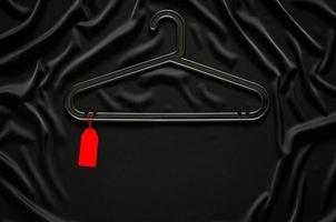 A black hanger with blank red price tag on black smooth and wavy cloth with space for text. Black Friday concept. photo