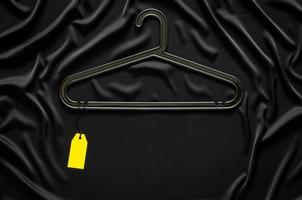 A black hanger with blank yellow price tag on black smooth and wavy cloth with space for text. Black Friday concept. photo