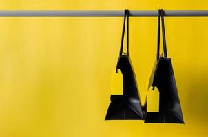 Black shopping bags with blank yellow price tags hanging on cloth rack with yellow background for Black Friday shopping sale concept. photo