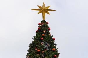 Star ornament puts on the top of big Christmas tree with colorful baubles and other ornaments. photo