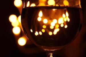 A glass of wine has the shadow of yellow and orange bokeh light on it which isolated on dark color background photo