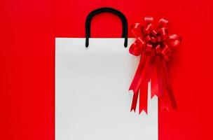White shopping bag with red bow and ribbon on red background. Black friday concept. photo