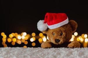 Brown teddy bear wearing santa claus hat with Christmas lights background. photo