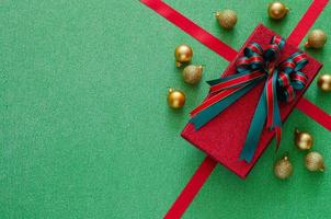 caja de regalo roja con cinta de lazo y adornos de adornos navideños sobre fondo verde. concepto de navidad y año nuevo. foto