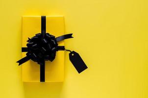 una caja de regalo amarilla con cinta negra y una etiqueta de precio en blanco se pone sobre fondo amarillo. concepto de viernes negro y día de boxeo. foto