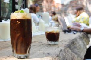 The espresso coffee with ice cube that mixing sweeten soft drink to enjoy hot weather of the summer with the background of cafe with old brick wall photo