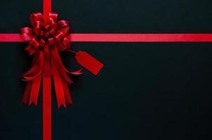 Red ribbon with bow and price tag on black background. Black friday concept. photo