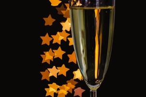 Partial focus of a glass of sparkling wine with golden star shape bokeh lights on dark background. photo