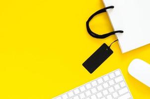 teclado y mouse inalámbricos con bolsa de compras para compras en línea con fondo amarillo. concepto de lunes cibernético y viernes negro. foto