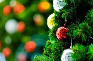 Red bauble and other ornament hanging on Christmas tree with bokeh background from another bigger Christmas tree. photo