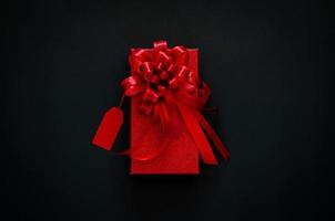 caja de navidad roja con cinta de lazo rojo y etiqueta de precio sobre fondo negro. concepto de viernes negro. foto