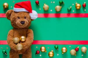 Smiling teddy bear holding Christmas baubles on blurred green background with ornaments. Christmas and New year concept. photo