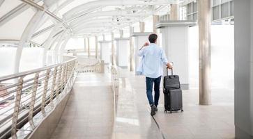 The back view of man holding a cup of coffee and pulling the luggage while he is waiting his friend at the airport. photo