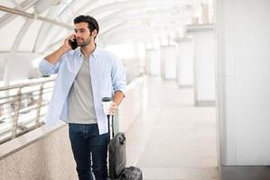 The man using the smartphone while the other hand holding a cup of coffee and pulling the luggage at the airport. photo