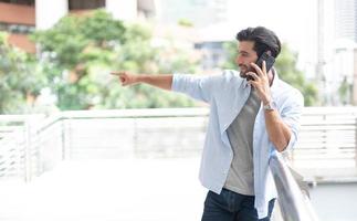 Businessman pointing to something while using a smartphone to talk with his friend at the outdoor. photo