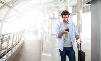 The man using the smartphone while the other hand holding a cup of coffee and pulling the luggage at the airport. photo