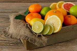 Assorted citrus fruits in a wooden box. Orange, tangerine, grapefruit, lemon and lime. On a wooden background photo