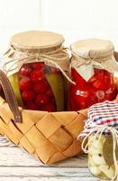 Homemade tomatoes preserves in glass jars in white wicker basket on wooden background photo