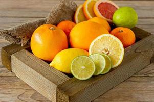 Assorted citrus fruits in a wooden box. Orange, tangerine, grapefruit, lemon and lime. On a wooden background. photo