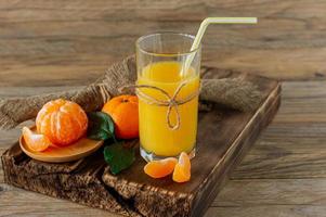 vaso de jugo de mandarina fresca con mandarinas maduras sobre tabla de madera foto