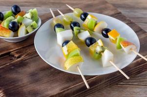 fruit vegetarian canape at skewers with grapes, kiwi and mango at wooden background. catering snack photo