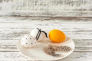 Trendy colored easter eggs in dark colors and feathers on a plate on wooden table. Preparation for easter holidays. Fesstive composition. photo