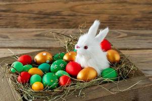 composición festiva de pascua con un pequeño conejito sentado en una caja de madera con huevos de pascua. concepto de estilo rústico, ecológico y granjero foto