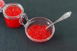 Red caviar in glass jar with silver spoon . Sea food. Healthy eating. Diet. black background. photo
