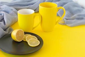 Two yellow mugs and sliced lemon on black plate with copy space. Trendy colors of the year 2021. Illuminating yellow and ultimate grey photo