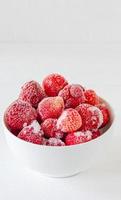 Frozen strawberry in white bowl on a wooden table. berries covered with hoarfrost photo