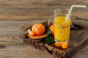 Glass of fresh tangerine juice with ripe tangerines on wooden board photo