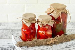 Glass jars with canned tomatoes with garlic and pepper. Fermented food on a white wooden background photo