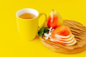 taza de jugo de pera y peras maduras sobre tabla de cortar de madera y fondo amarillo con espacio para copiar.