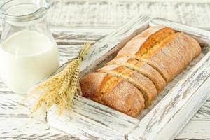 Sliced ciabatta bread on wooden cutting board next to jug with milk. Tasty food close up. Homemade baked bread photo