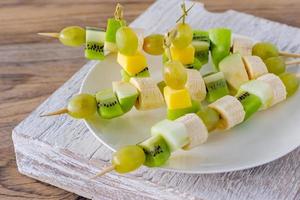 conjunto de canapés con frutas, bayas en plato blanco sobre fondo de madera foto