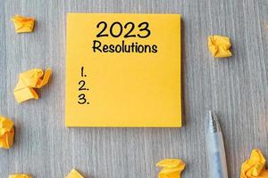 2023 RESOLUTIONS word on yellow note with pen and crumbled paper on wooden table background. New start, Strategy and Goal concept photo